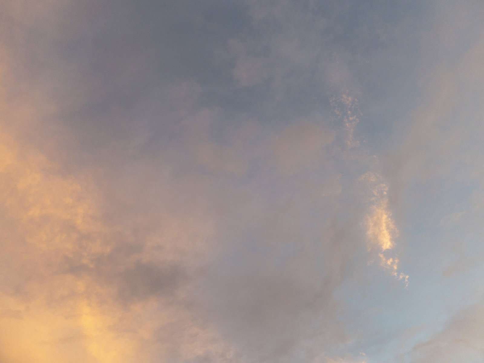 オレンジとグレーの夕焼け空に薄雲が広がる黄昏時の風景