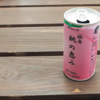 木目のテーブルに置かれた桃の恵み缶のジュースの写真