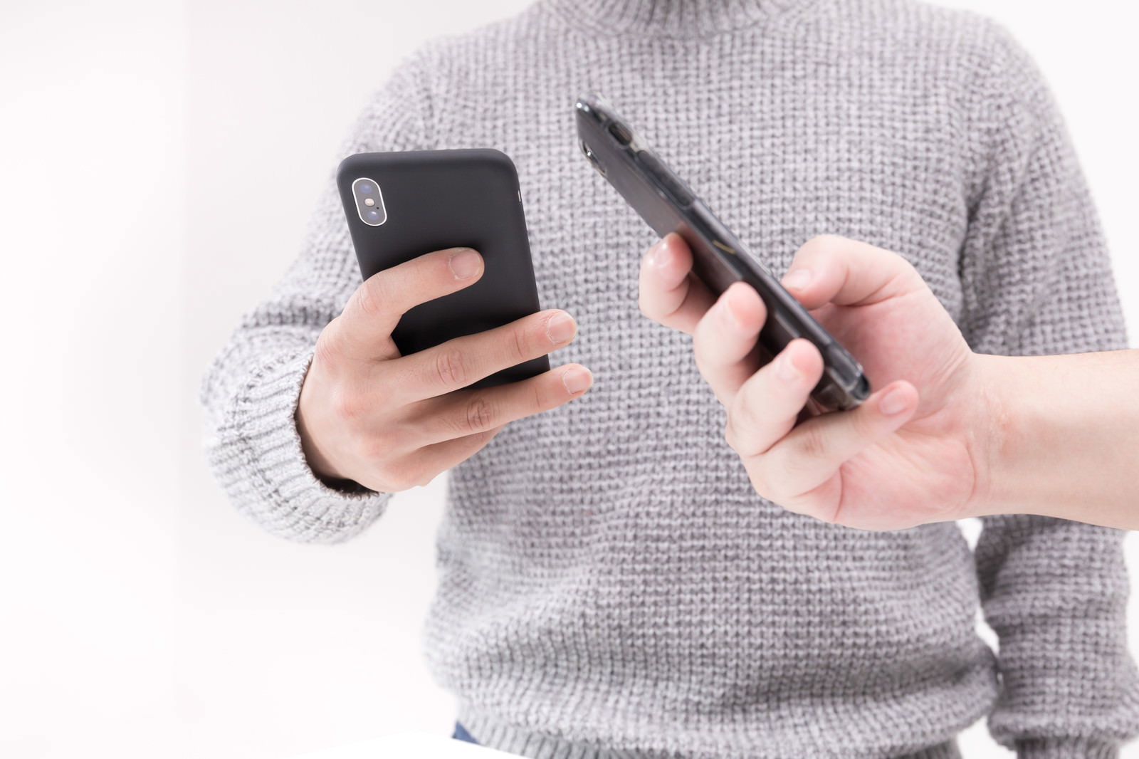 グレーのセーター姿の人が両手にスマートフォンを1台ずつ持っている