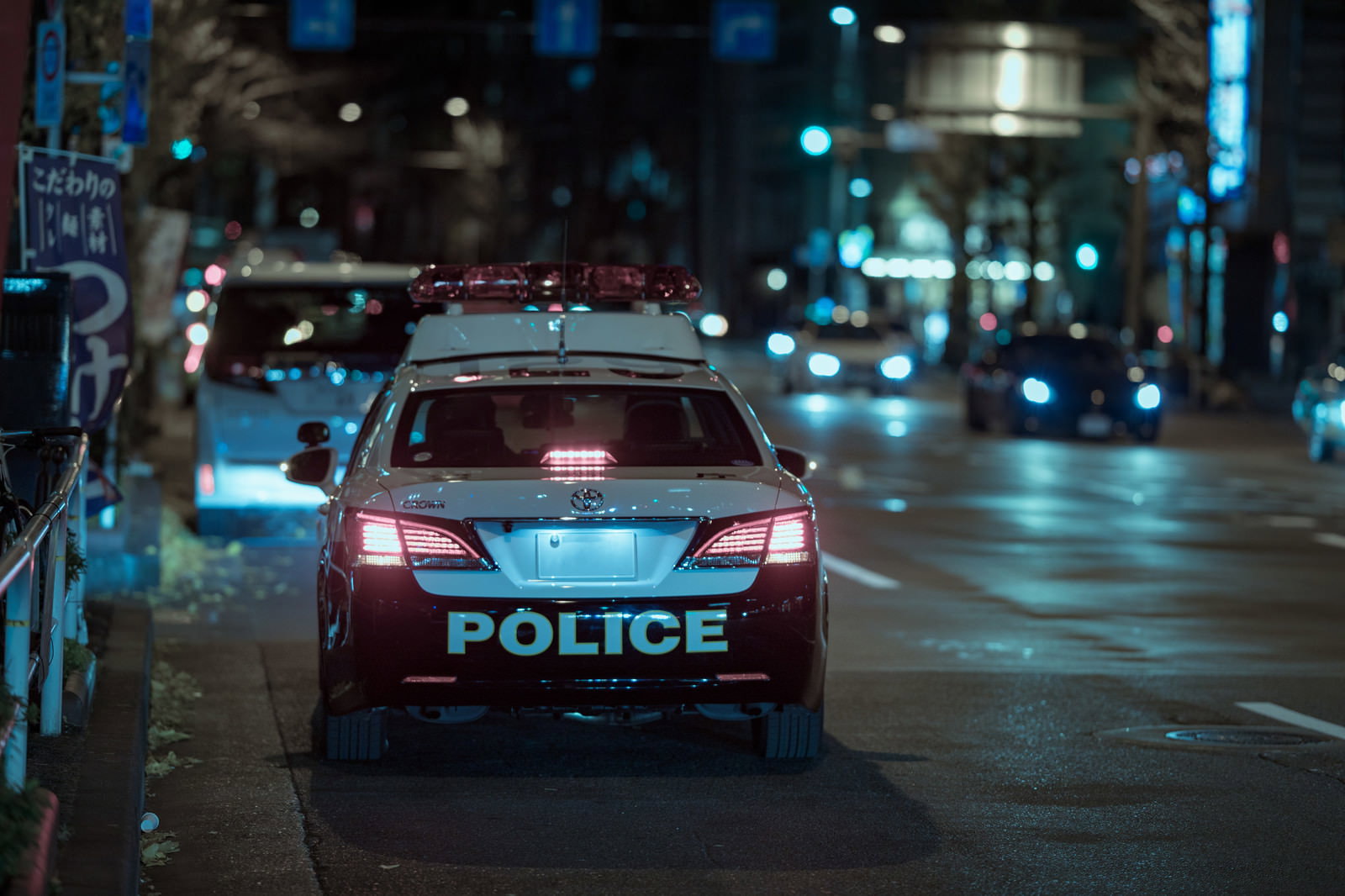 夜の街の道路を青いライトを光らせながらパトロール中のパトカー