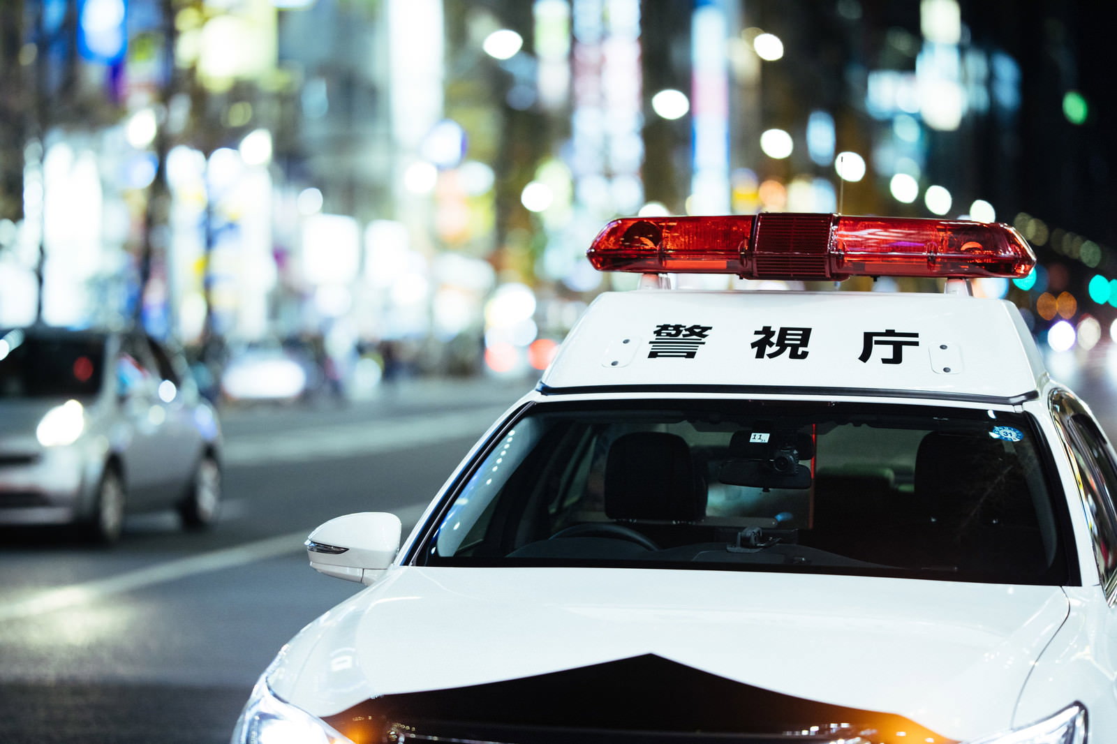 夜の繁華街でネオンの光に照らされて停車するパトカー