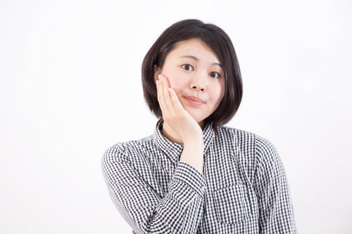 歯痛ポーズで盛れると聞いて、片手を頬に当てる女性