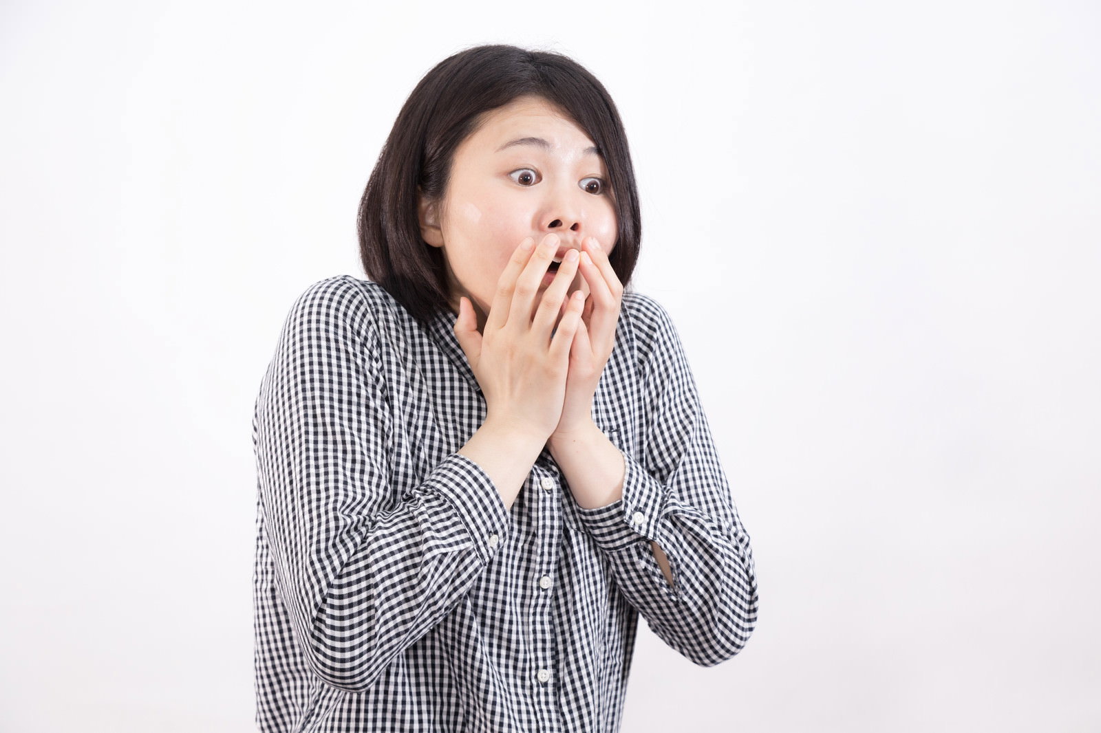 チェック柄のシャツを着た女性が両手で口元を覆って驚いている様子［モデル：佐竹PP］