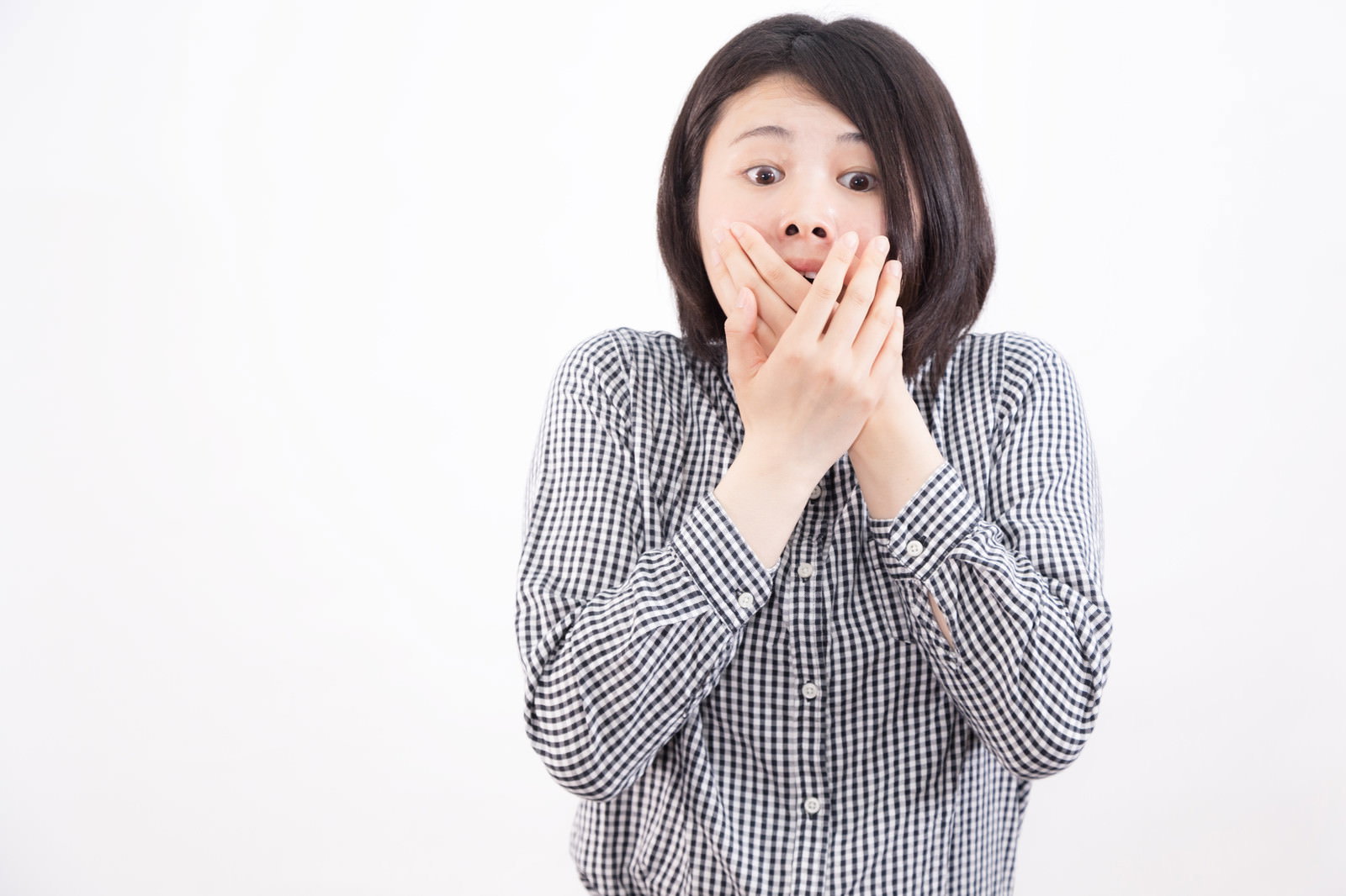 チェック柄のシャツを着た女性が両手で口を覆って驚いている表情［モデル：佐竹PP］