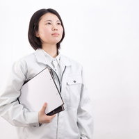 書類ファイルを持つグレーの作業着姿の女性作業員の写真