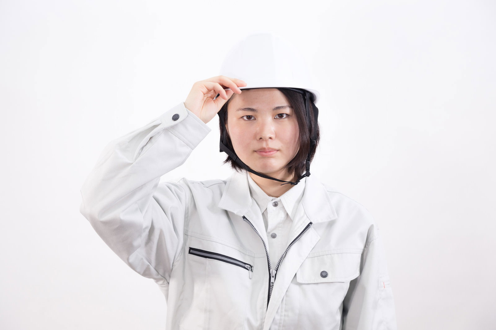 白いヘルメットとグレーの作業服を着た女性が片手を額にかざしている［モデル：佐竹PP］