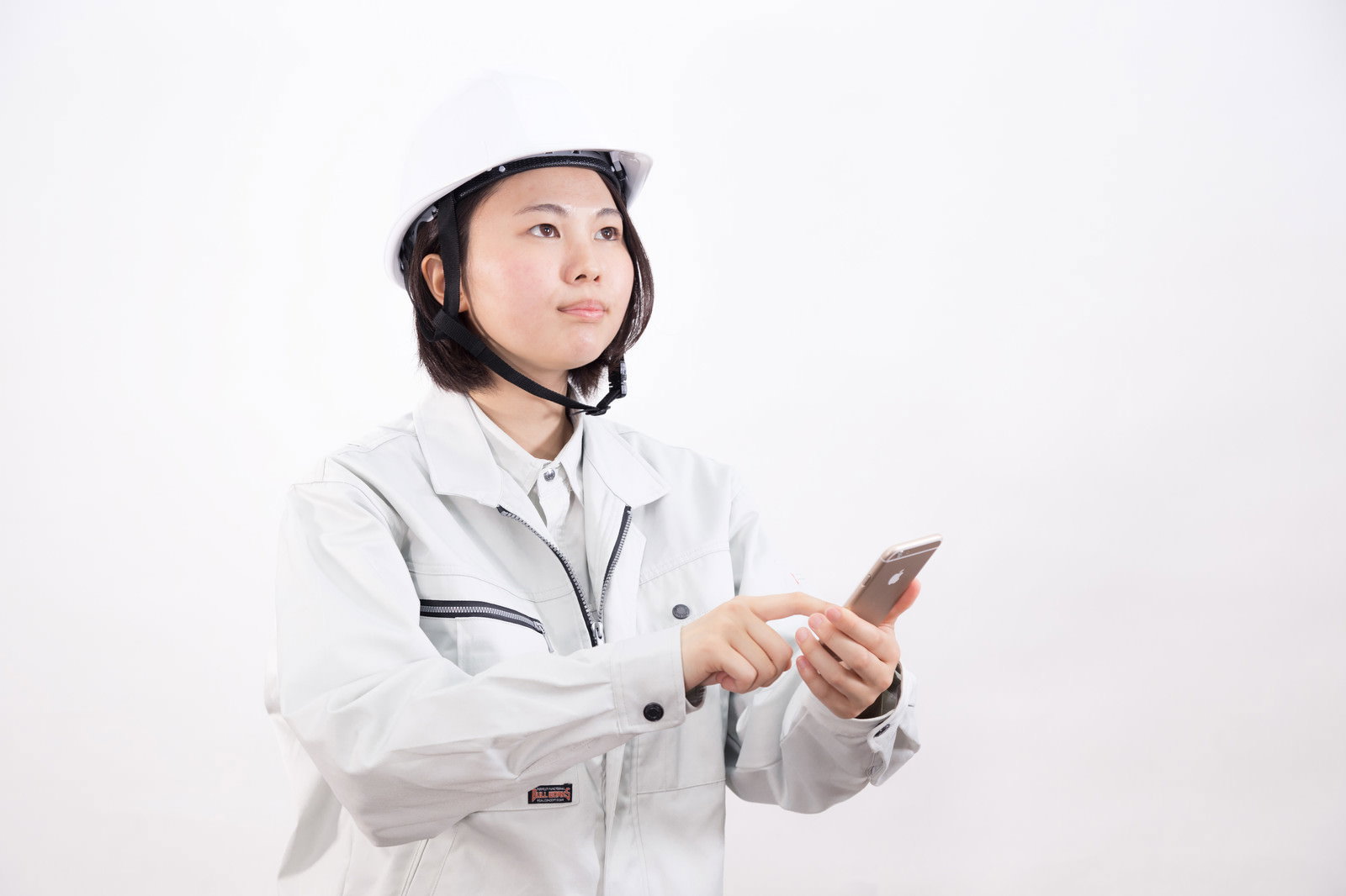 白いヘルメットと作業着を着た女性がスマートフォンを操作している［モデル：佐竹PP］