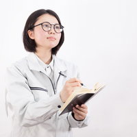 白い作業着でクリップボードにメモを取る研修生の写真
