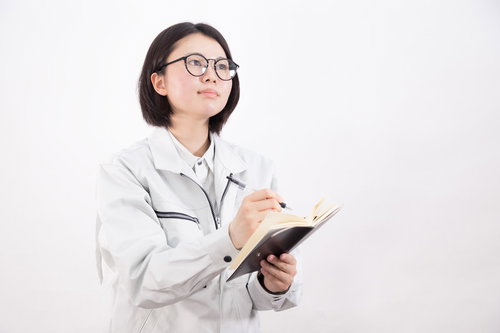 白い作業着でクリップボードにメモを取る研修生