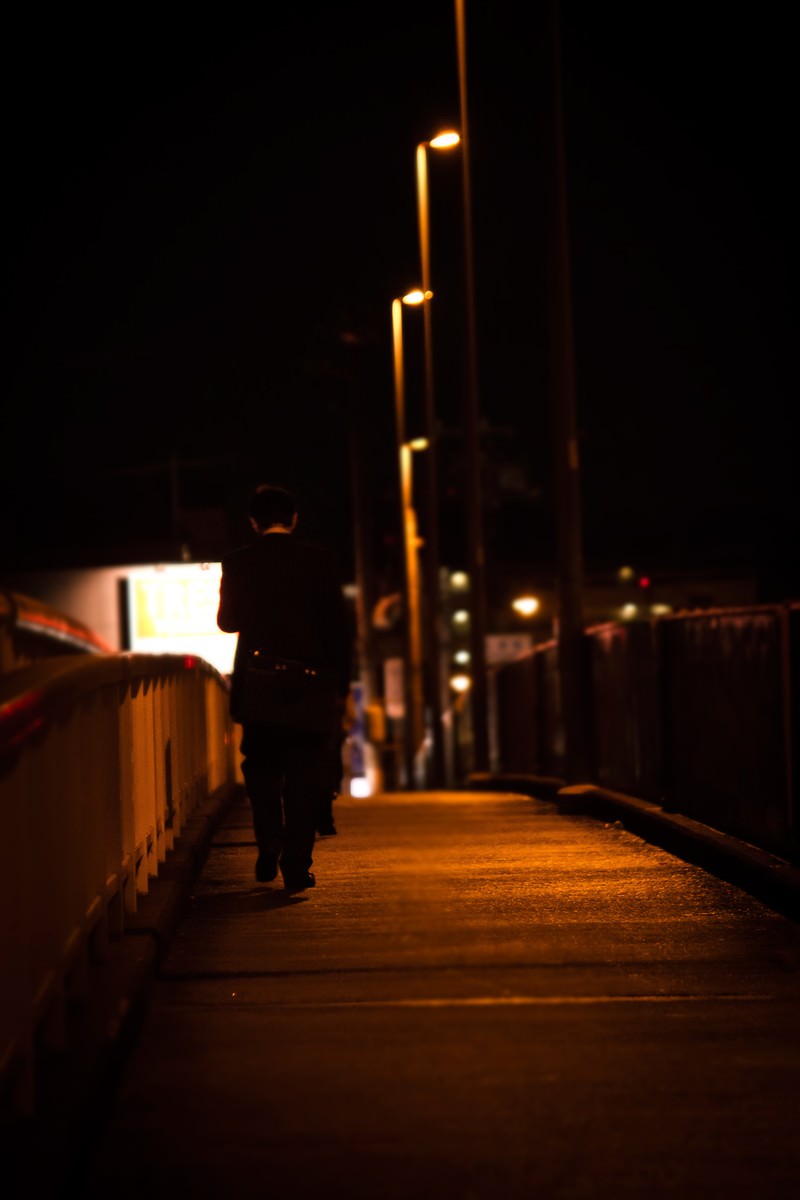 夜の歩道を歩くサラリーマンの後ろ姿
