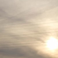 電線が横切る曇り空と太陽の夕暮れの写真