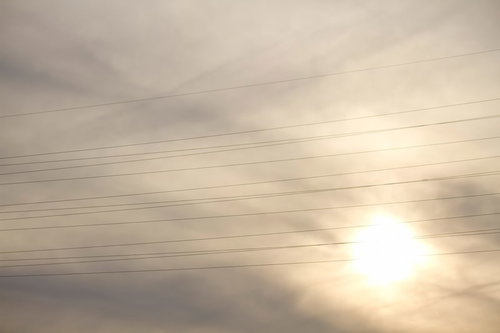 電線が横切る曇り空と太陽の夕暮れ