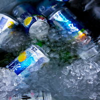 暗い室内で氷に埋もれて冷えるビールの缶の写真