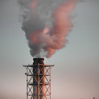 赤く染まる排煙をあげる工場の煙突と大気汚染の写真