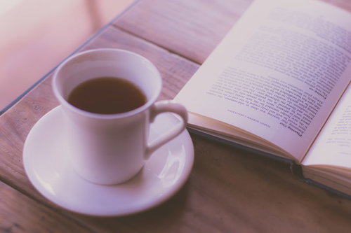 白いカップのコーヒーと開かれた洋書、木製テーブル