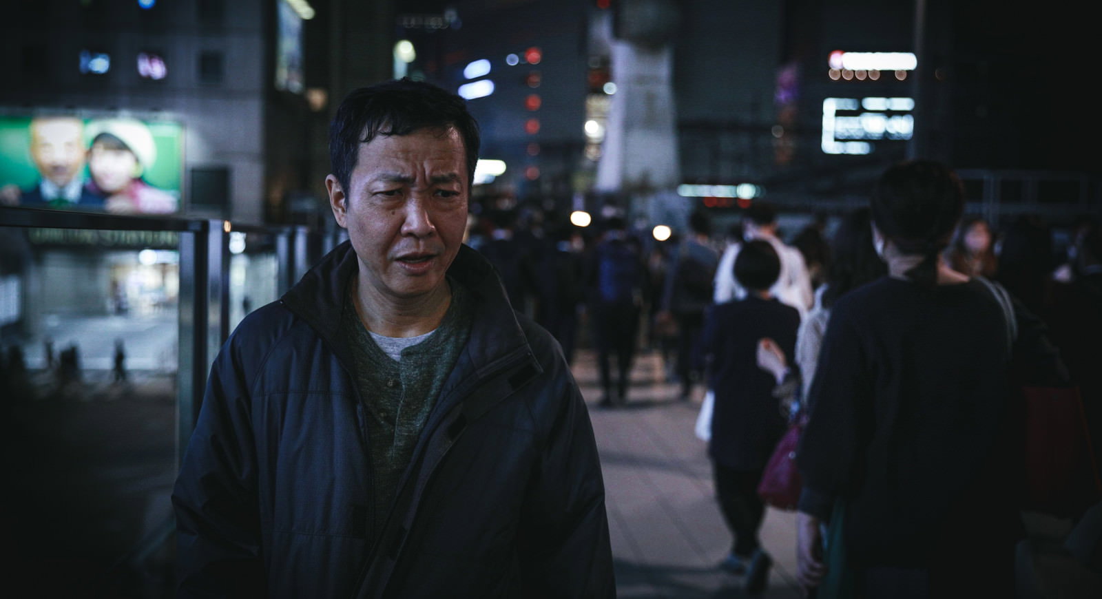 夜の繁華街で憂鬱そうな表情を浮かべる中年男性［モデル：のせさん］