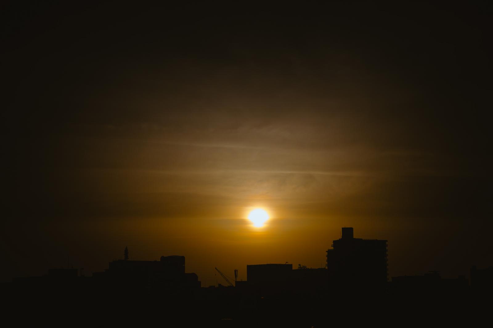 街のシルエットの上に昇る輝く太陽と朝焼けの空