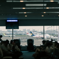 空港ロビーの窓から見える駐機中の旅客機と待合室の乗客の写真