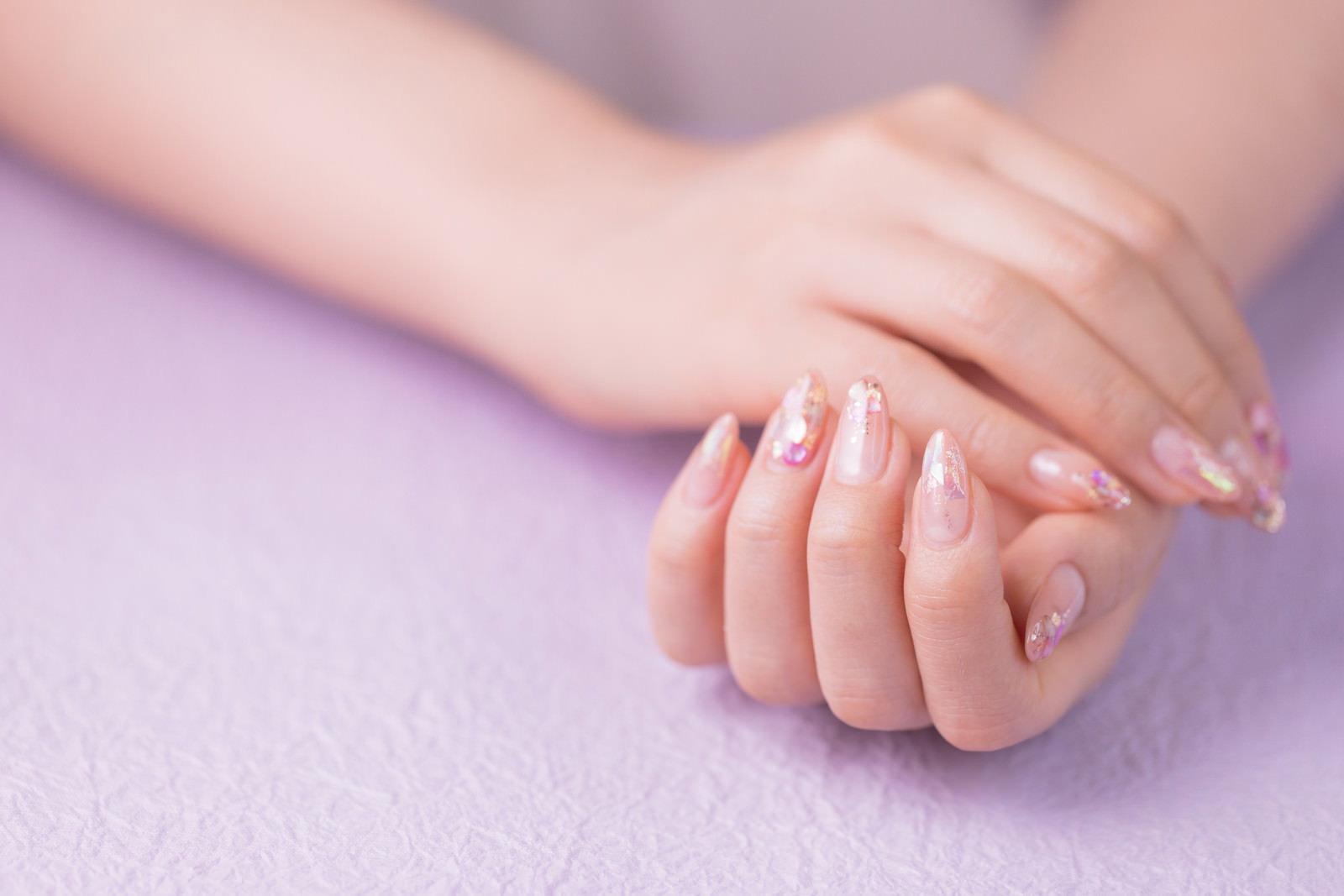 薄紫色の背景にキラキラネイルをした女性の両手を重ね合わせた様子