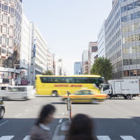 都心の車道を走る黄色いはとバス、高層ビルと交通風景の写真