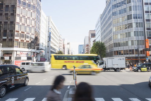 都心の車道を走る黄色いはとバス、高層ビルと交通風景