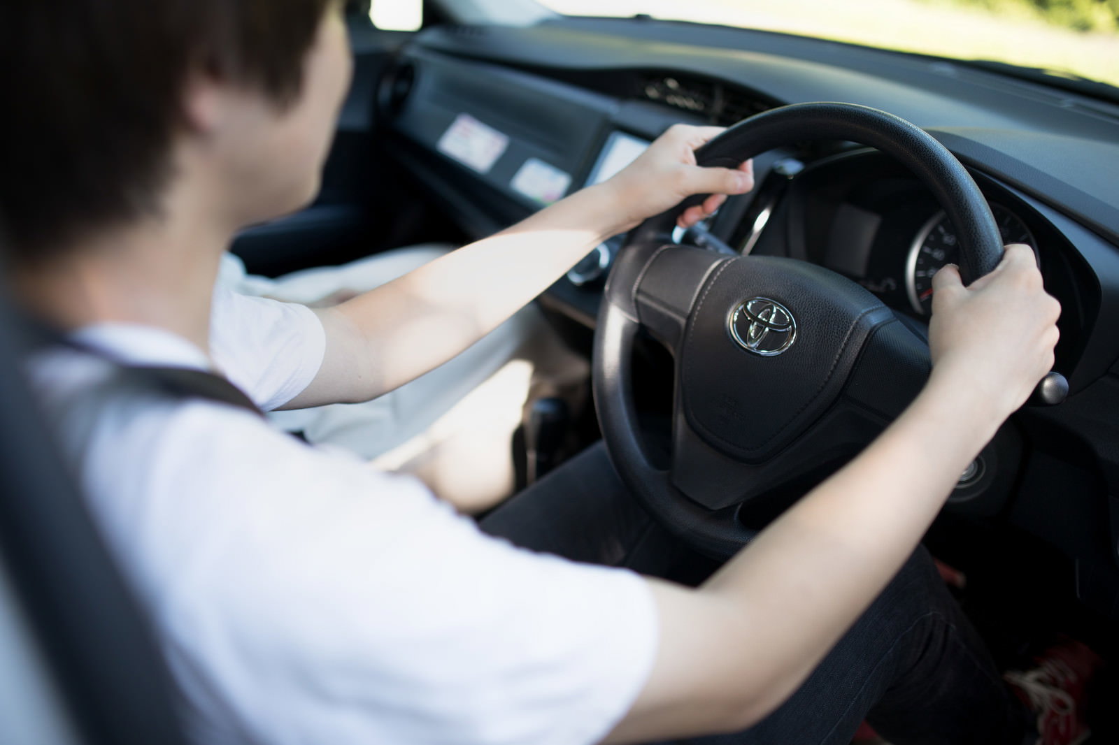 白いシャツを着た男性が乗用車のハンドルを握って運転している様子