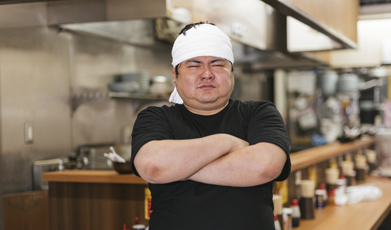 白いコック帽をかぶり腕組みをするラーメン屋の男性店主［モデル：段田隼人］