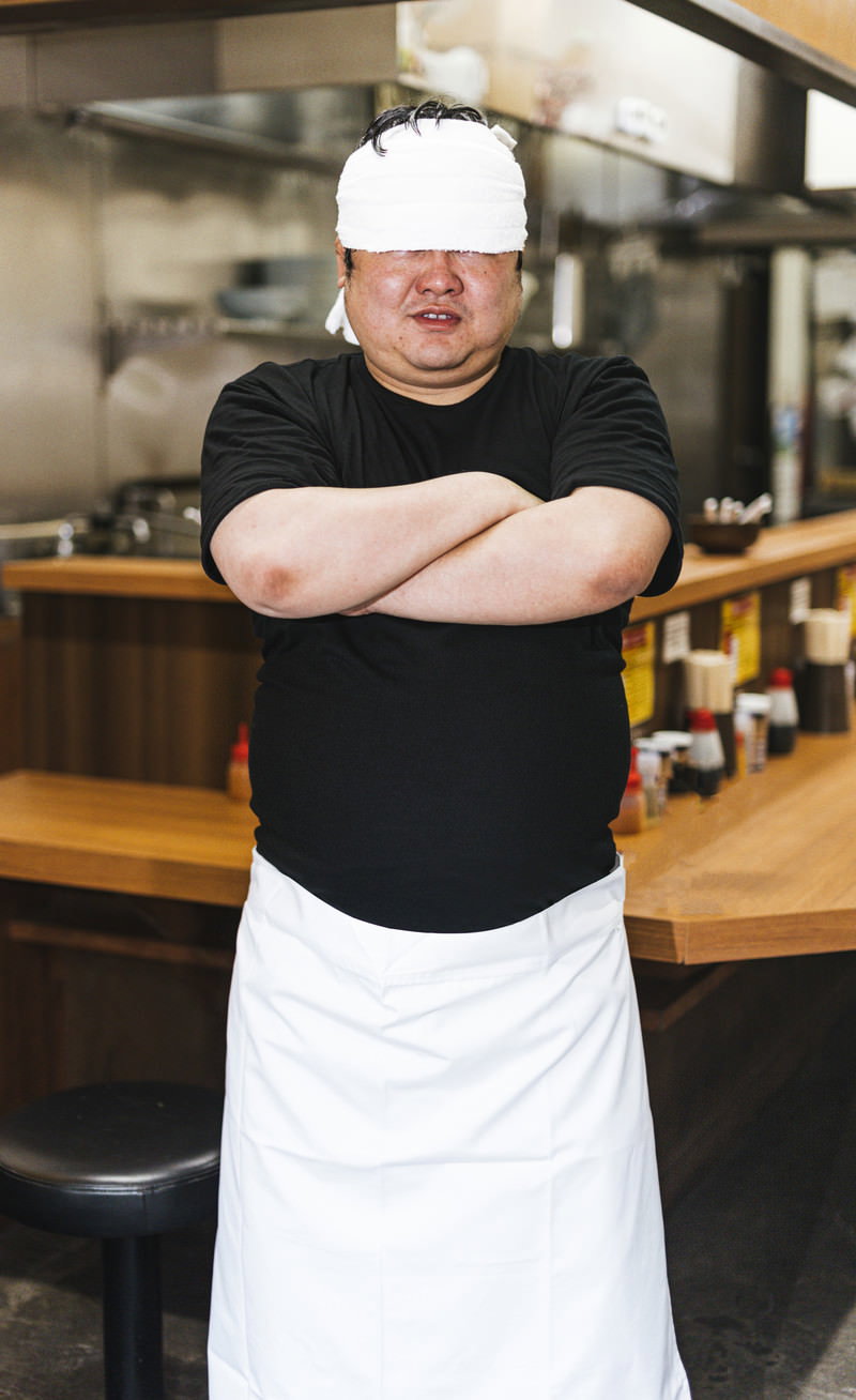 白いコック帽を被り腕組みでドヤ顔を決める目隠しラーメン店員［モデル：段田隼人］