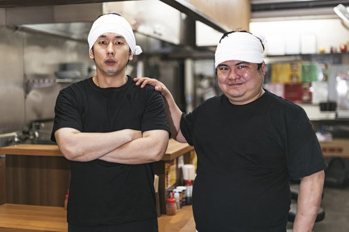 期待の新人を紹介するラーメン店主と弟子の厨房での一枚