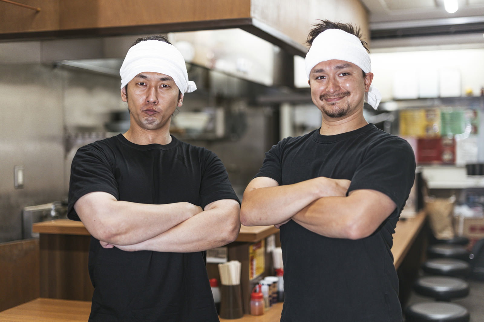 ラーメン屋の厨房で腕組みをして立つ二人の男性店員［モデル：大川竜弥 Max_Ezaki］