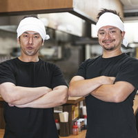ラーメン屋の厨房で腕組みするアルバイトのふたりの写真