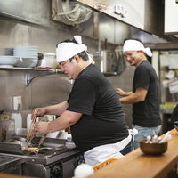 厨房で調理する割腹のいいラーメン店主の調理風景の写真