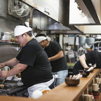 ピークタイムが落ち着いた夜のラーメン屋の厨房で調理する男性店員の写真