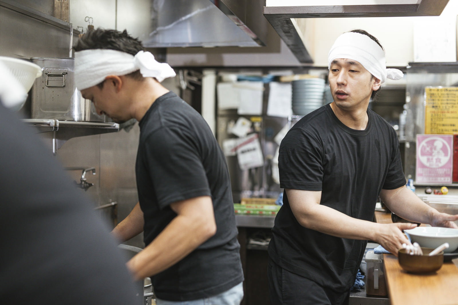 ラーメン店の厨房で先輩から調理を学ぶ新人アルバイトの男性2人［モデル：大川竜弥 Max_Ezaki］