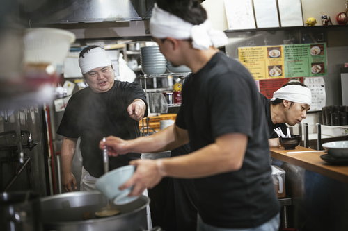 厨房でアルバイトに調理指導するラーメン屋の大将