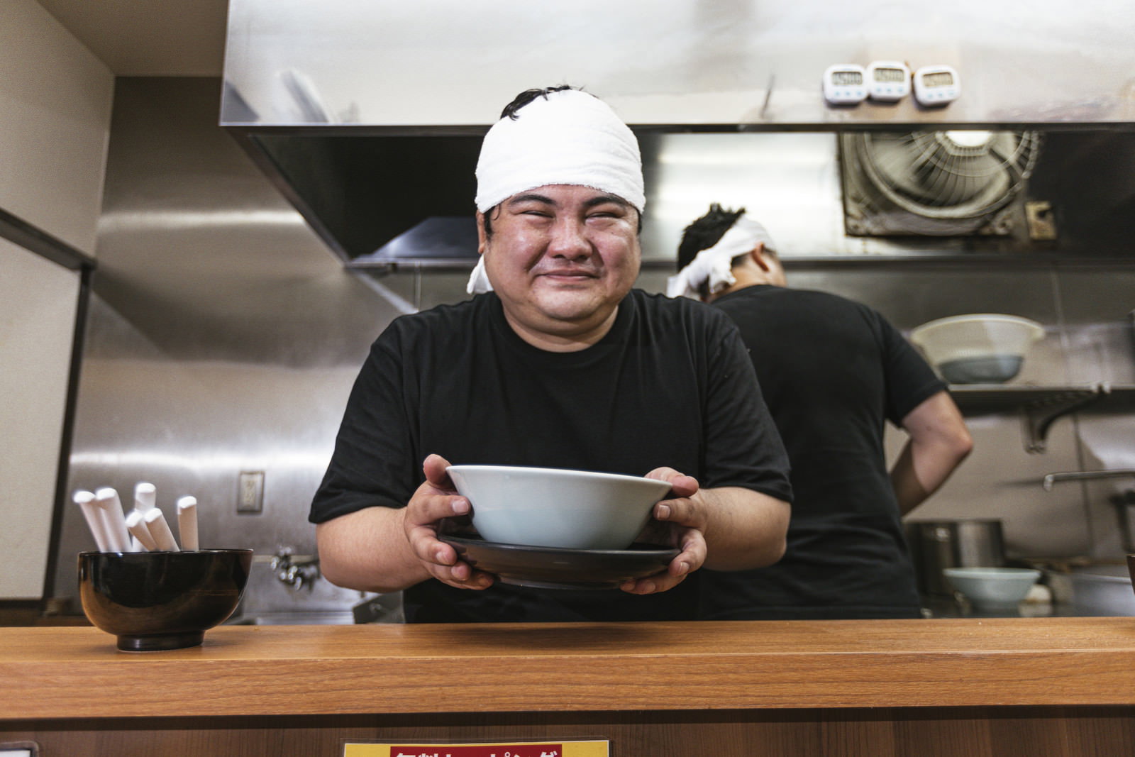 ラーメン店の厨房で白い帽子とエプロンを着けて働く男性店員［モデル：段田隼人］