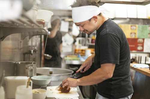 ラーメン屋の厨房でチャーシューを切る店員