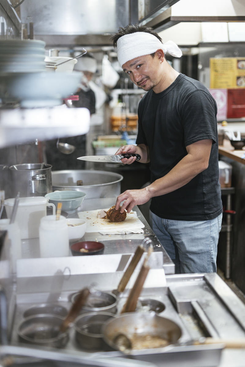 ラーメン屋の厨房で調理をする白い帽子の外国人男性店員［モデル：Max_Ezaki］