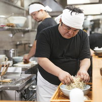 白い帽子とエプロン姿で麺をほぐすラーメン屋の大将の写真