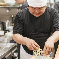 白い帽子をかぶるラーメン店主が厨房で麺を茹でるの写真