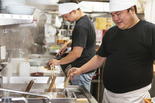 麺の湯で加減をこまめにチェックするラーメン店の男性店員