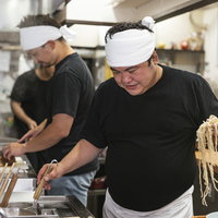 麺を片手にテボをチェックする厨房の男性店主の写真