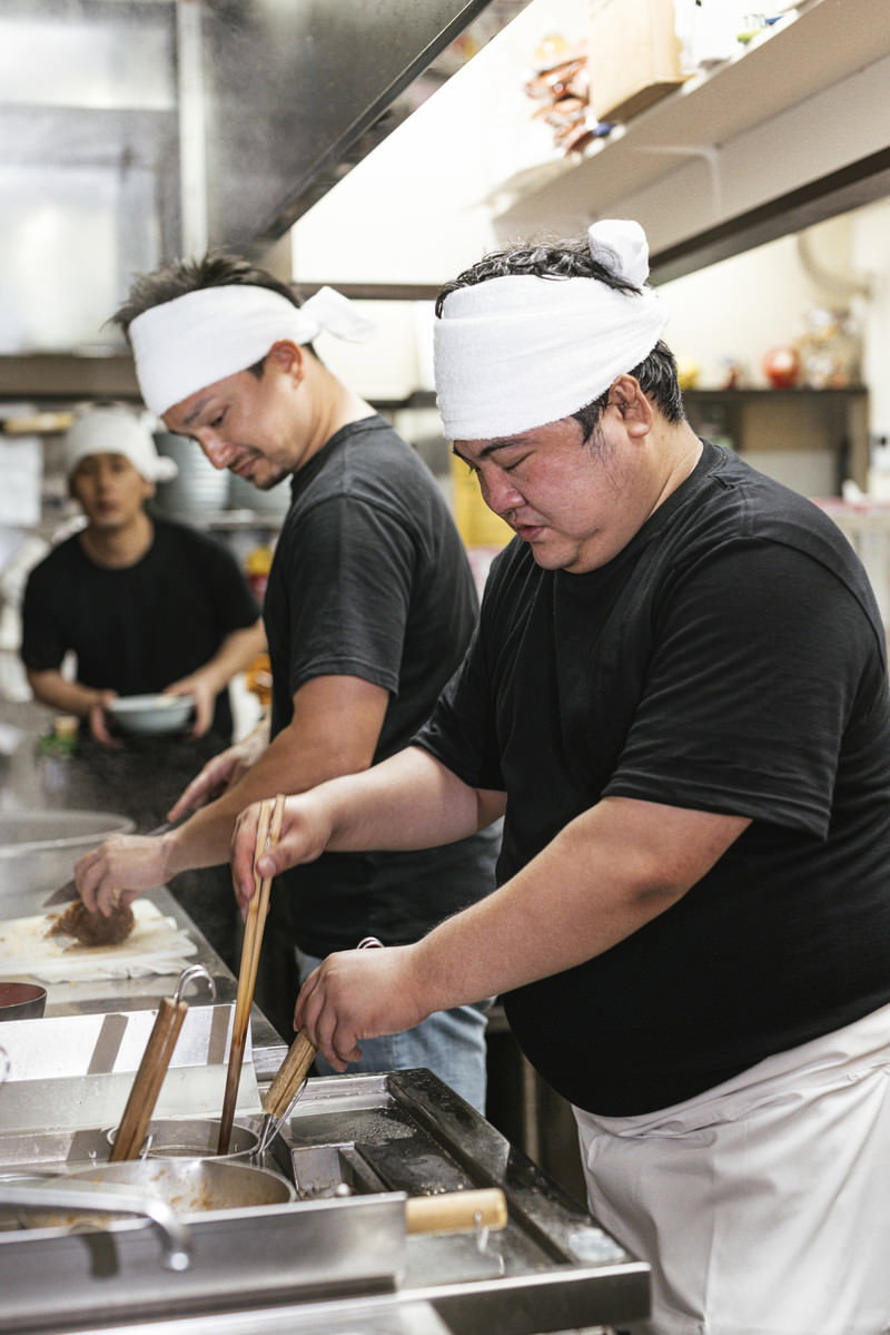 厨房で麺を茹でる作業をする白衣とコック帽姿の男性店員［モデル：段田隼人 Max_Ezaki 大川竜弥］