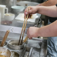 麺が固まらないようにテボで箸をほぐす男性の手の写真