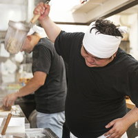 白いキャップのラーメン店主が厨房で披露する独特な湯切りの写真