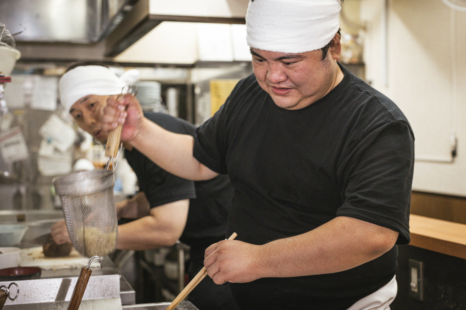 ラーメン店の厨房で湯切り作業を心配そうに見つめる新人アルバイト［モデル：段田隼人］