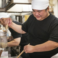 ラーメンの湯切りをする様子を心配そうに覗き込む新人アルバイトの写真