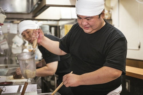 ラーメンの湯切りをする様子を心配そうに覗き込む新人アルバイト