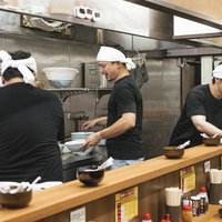 ラーメン屋の厨房で働く3人の男性店員が調理作業をする様子の写真