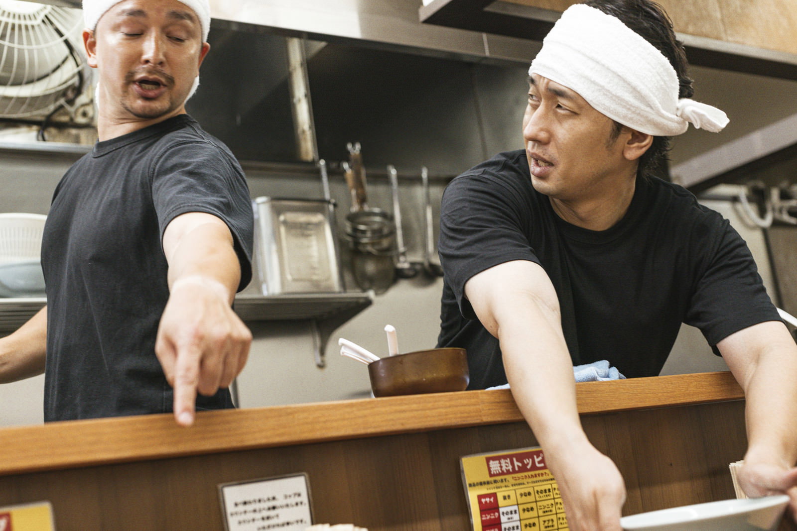 厨房で白い帽子をかぶった男性店員が後輩に指導している様子［モデル：Max_Ezaki 大川竜弥］